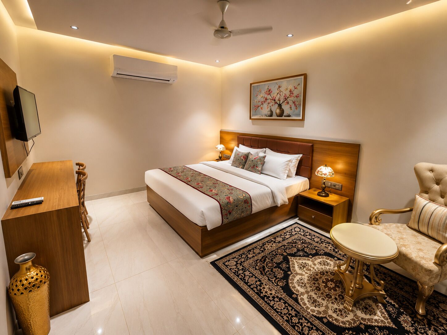 Habitación de hotel con cama, mesita de noche, lámpara, sillón, escritorio y televisor.