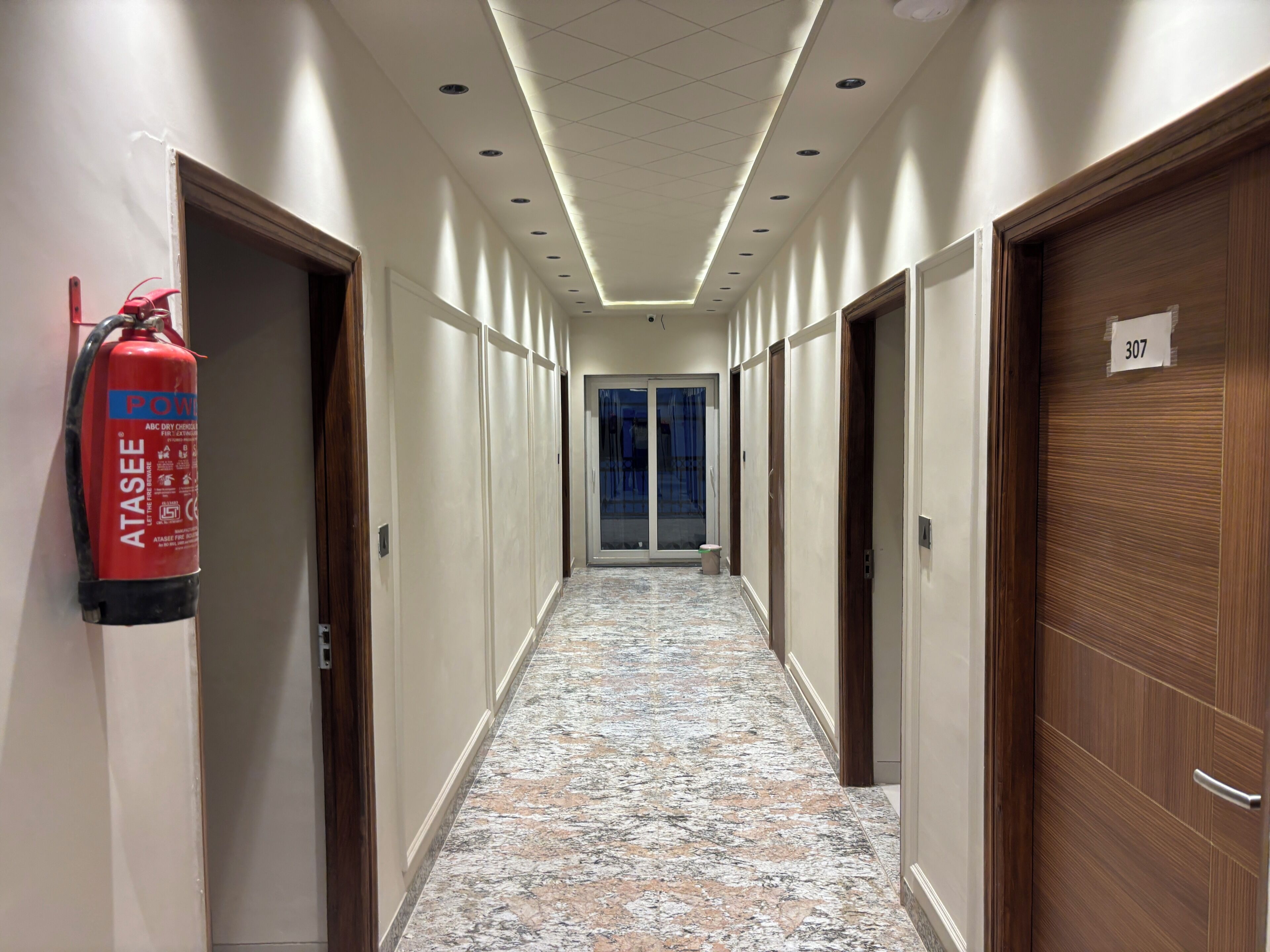 Pasillo de hotel con extintor, puertas numeradas 307 y piso estampado.