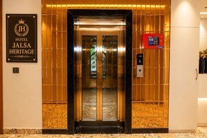 An elevator entrance with a sign for Hotel Jalsa Heritage, a control panel, and a decorative wall.