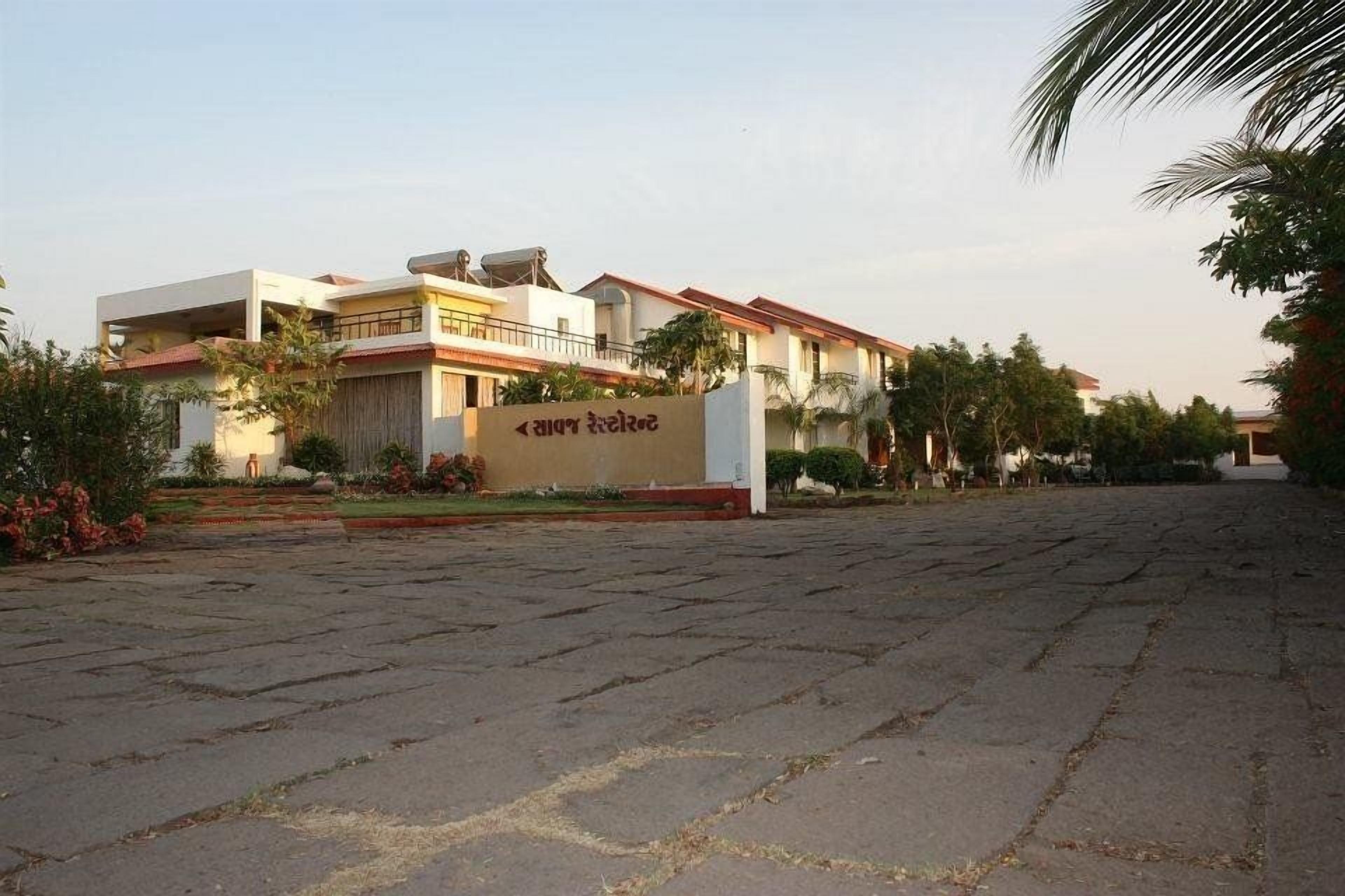 A building with a sign, paved courtyard, and surrounding greenery.