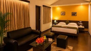 Habitación de hotel con cama, sofá, una mesita de centro con flores, lámpara y ventilador de techo.