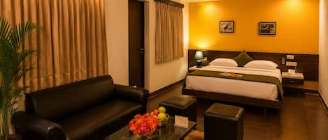 Habitación de hotel con cama, sofá, una mesita de centro con flores, lámpara y ventilador de techo.