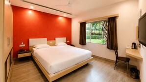 A hotel room with a bed, bedside tables, a TV, a desk, and a window with curtains. - Asiatic Pride Resort (Dhari)