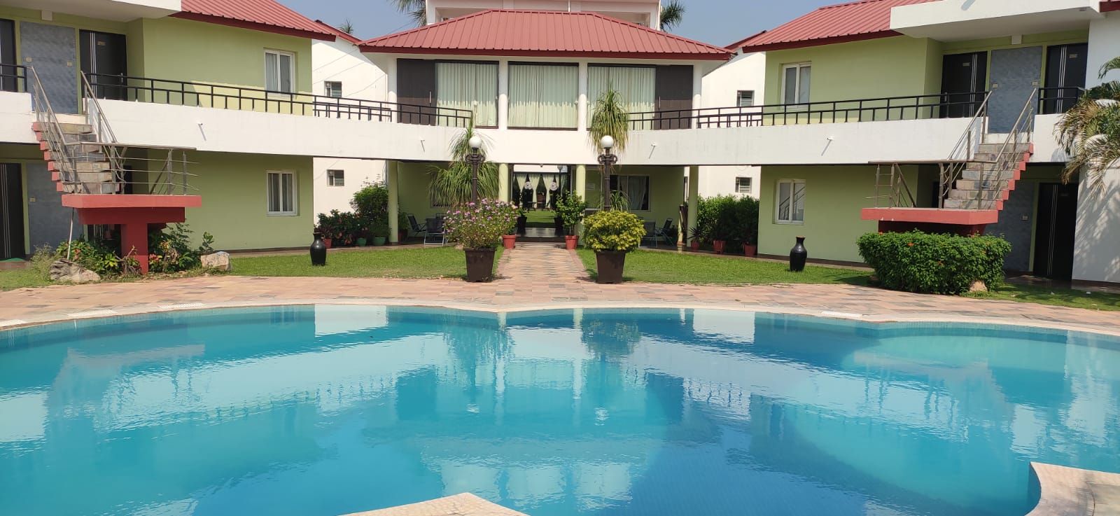 Um hotel com piscina, várias varandas e um jardim bem cuidado.