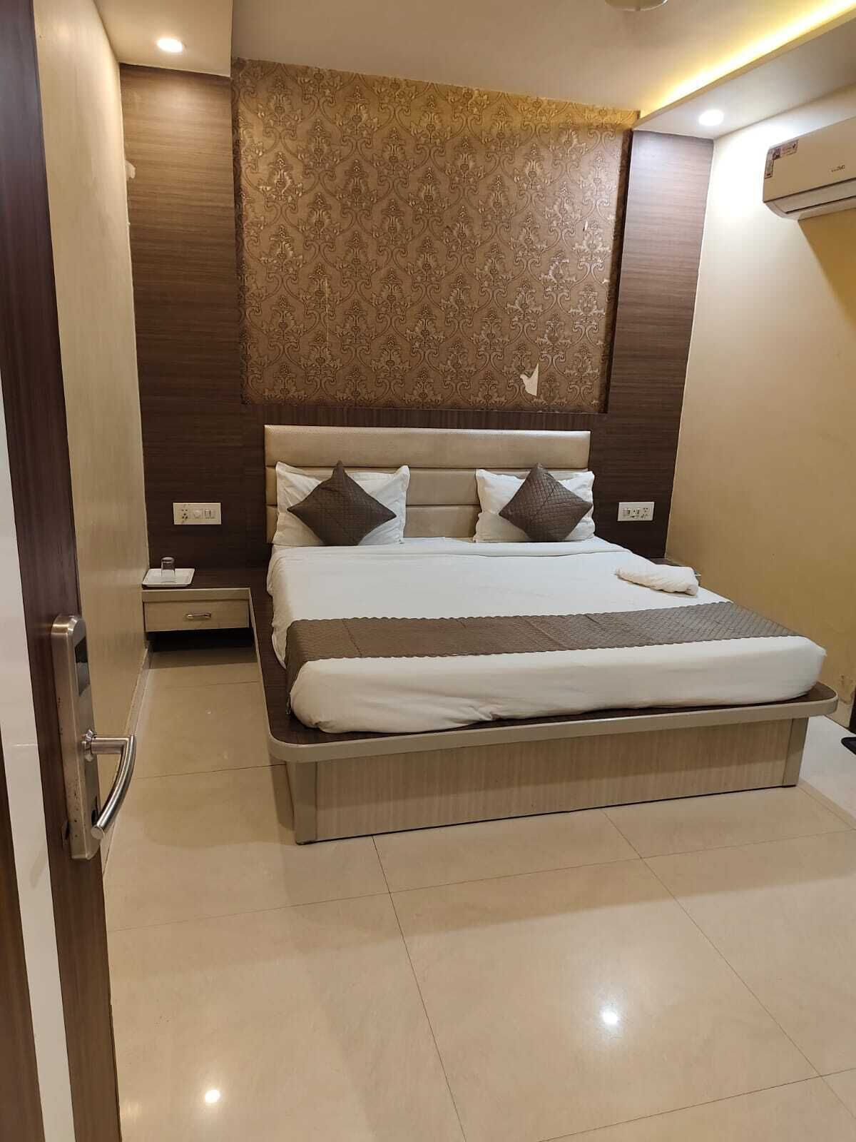A bedroom with a large bed, a nightstand, a wall-mounted air conditioner, and a patterned headboard.
