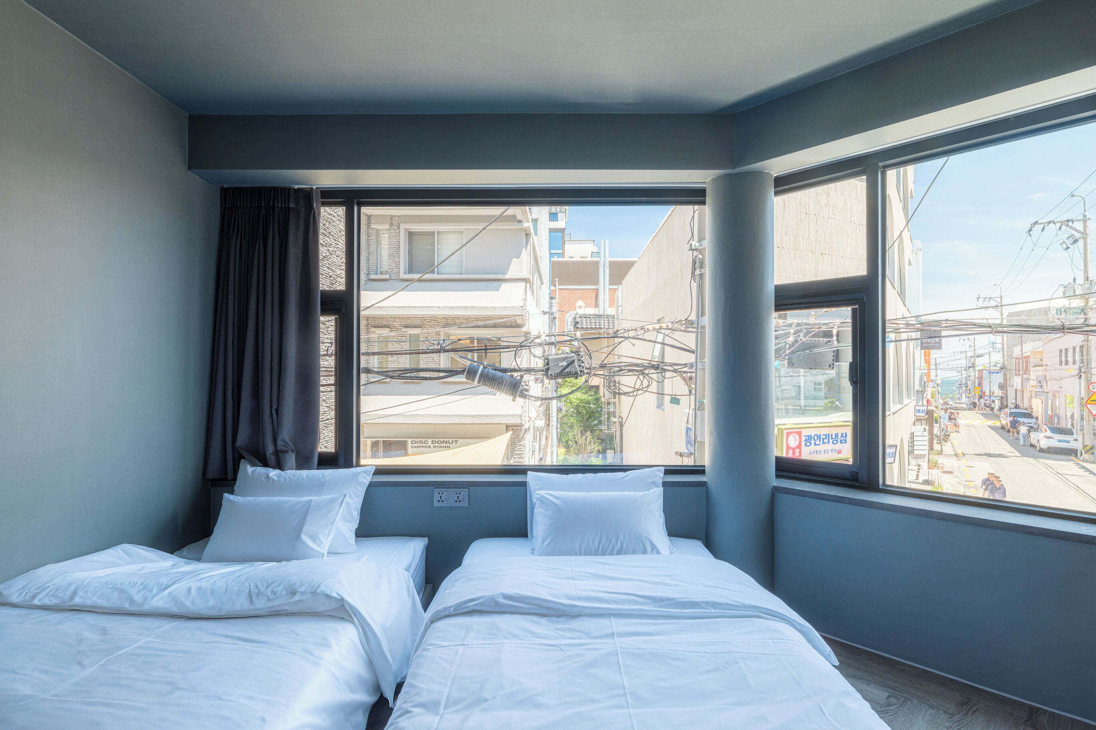 Habitación de hotel con dos camas, una ventana con vistas a la ciudad y un cartel de un puesto de café afuera.