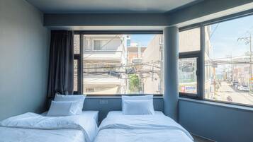 Habitación de hotel con dos camas, una ventana con vistas a la ciudad y un cartel de un puesto de café afuera.