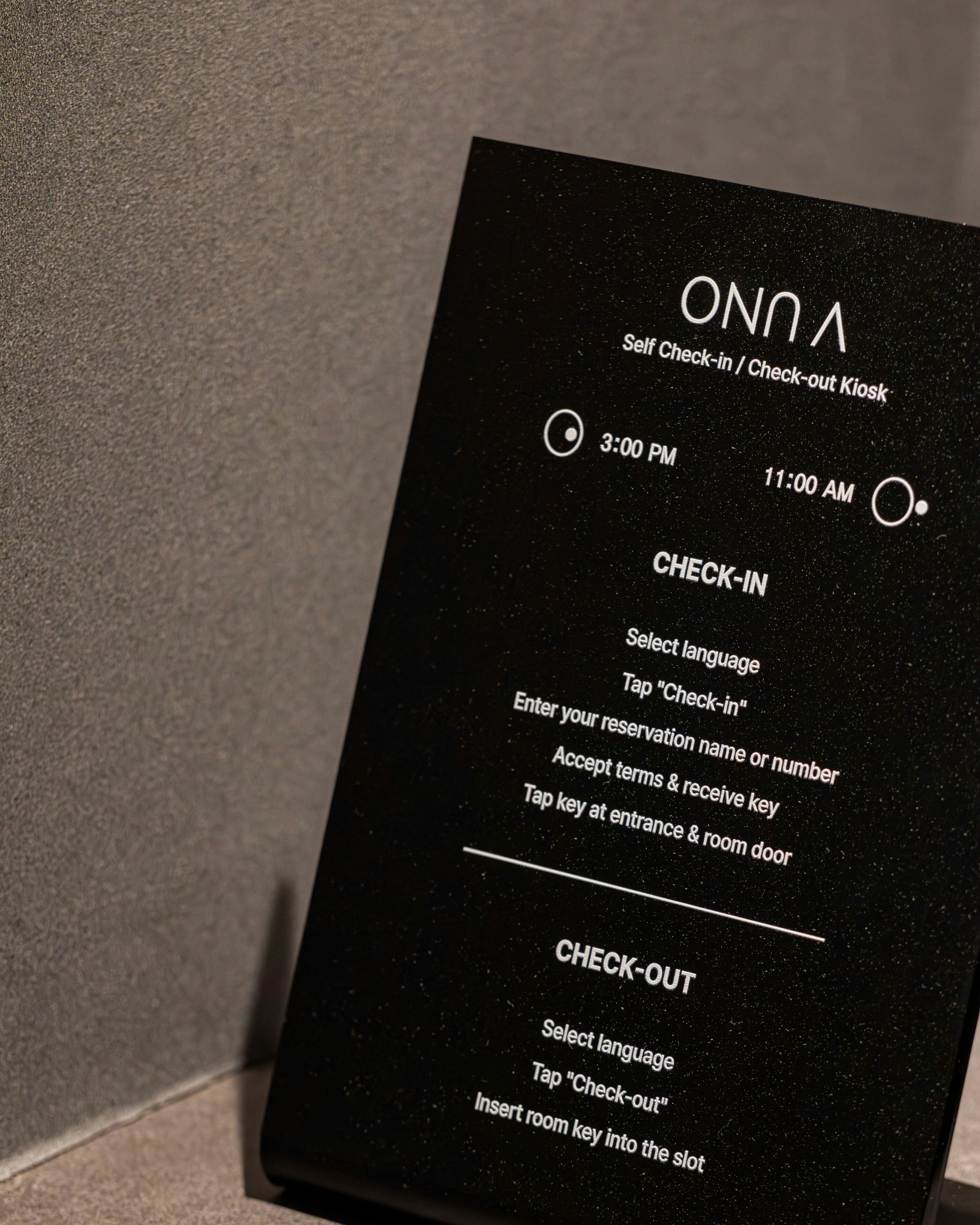A black kiosk sign with instructions for self check-in and check-out, including times and steps for both processes.