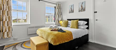 A modern bedroom with a bed, bedside tables, a bench, a window, and artwork on the wall.