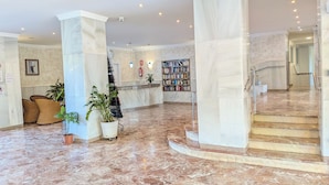 Eine Lobby mit Marmorboden, einem Empfangstresen, einem Bücherregal und einer Treppe.