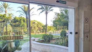Ein Hotel Eingang mit Glastür, einem Schild mit der Aufschrift 'SALIDA' und Blick auf einen Garten mit Palmen und einem Pool.