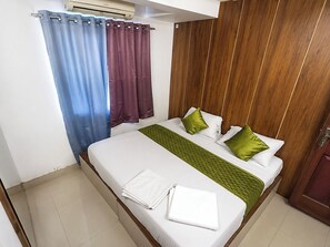 A hotel room with a bed, curtains, a wooden headboard, and a tiled floor.