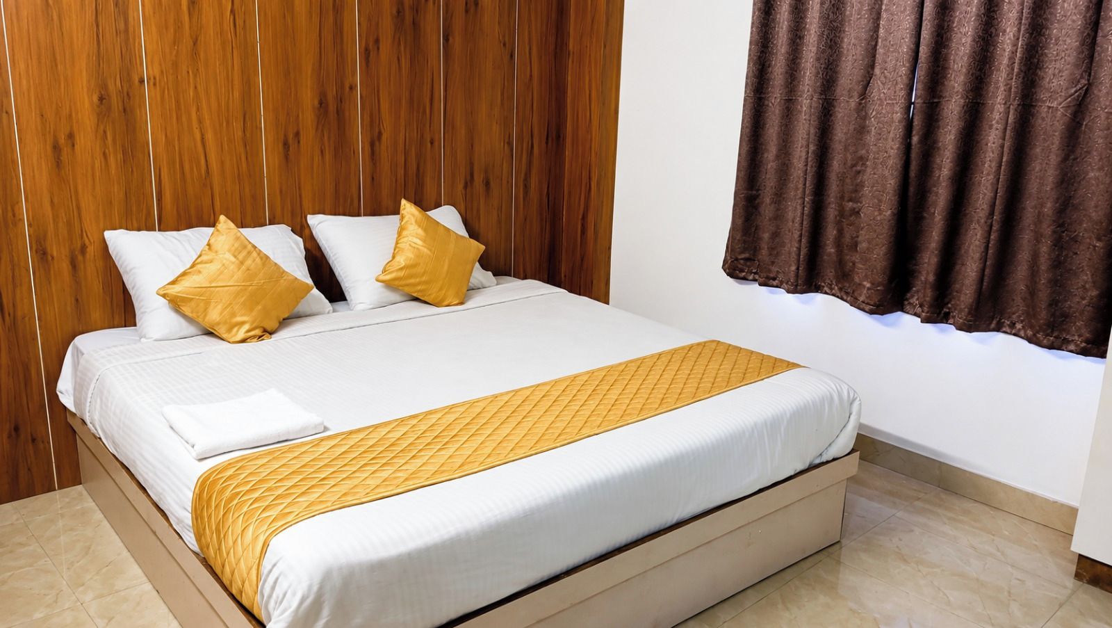 Una habitación de hotel con una cama, cabecera de madera y una ventana con cortinas.