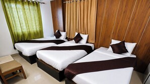 Quarto de hotel com quatro camas de solteiro dispostas em fila, um banco de madeira e uma pequena mesa.