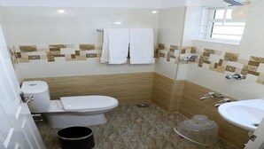 Casa de banho com sanita, bidé e lavatório, paredes em azulejo e janela.