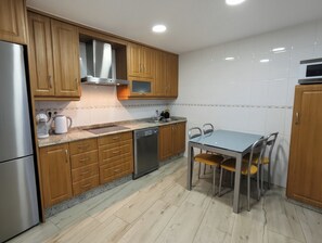A kitchen with wooden cabinets, a stainless steel refrigerator, a dishwasher, and a dining table with chairs.