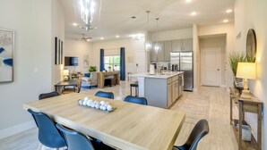 A modern kitchen with a central island, a dining area with a wooden table and blue chairs, and a living space with a sofa and a TV. - Palm Coast Escape: Bike Trails & Beach Days! (Palm Coast)