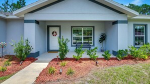 A residential house with a front porch, a door with a wreath, a bench, and small plants. - Palm Coast Escape: Bike Trails & Beach Days! (Palm Coast)
