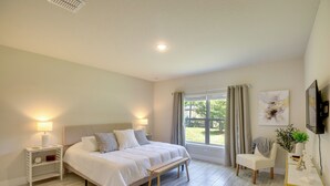 A bedroom with a bed, bedside tables, a bench, a chair, a desk, a TV, and a window with curtains. - Palm Coast Escape: Bike Trails & Beach Days! (Palm Coast)