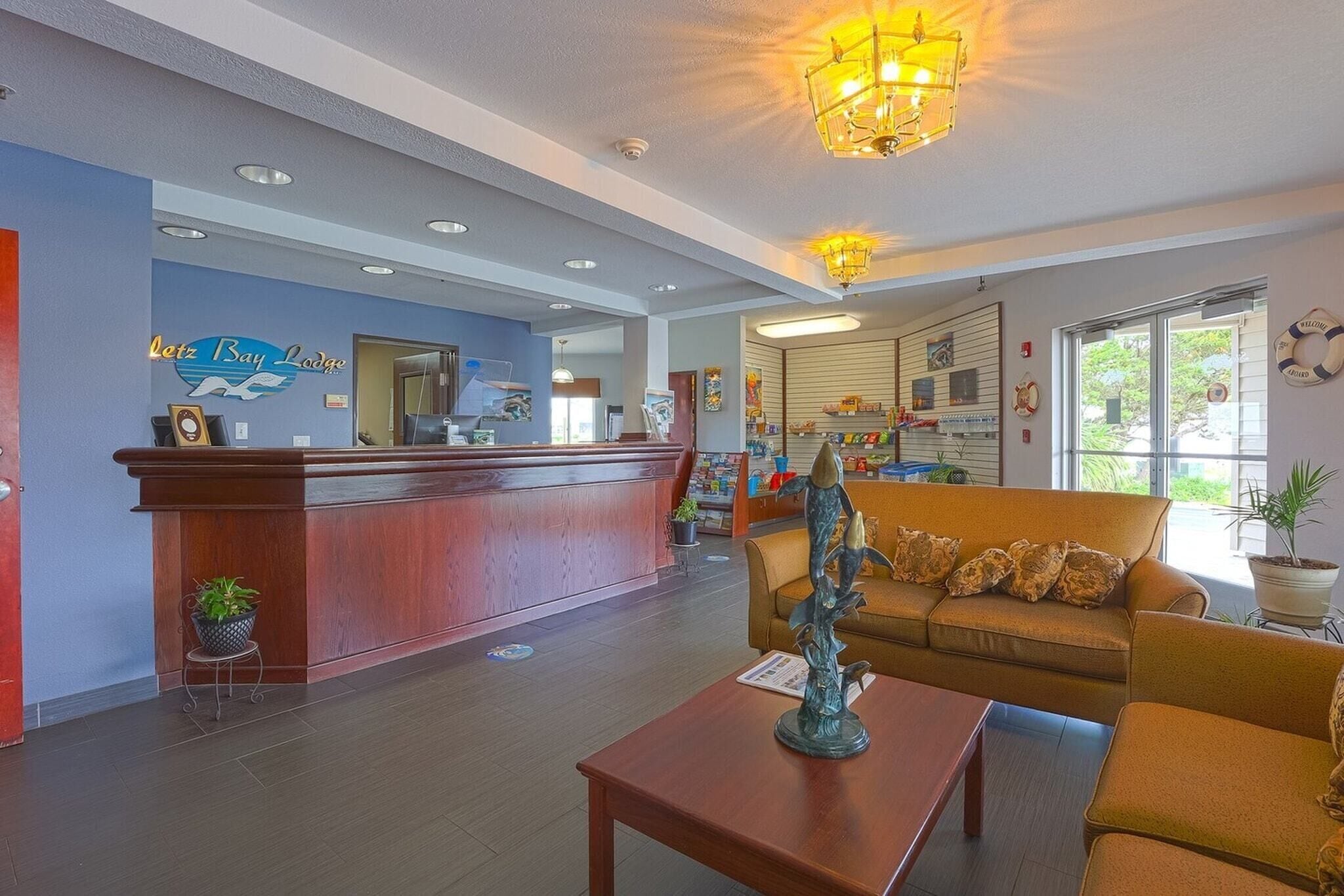 A reception area with a wooden desk, a blue wall with the hotel name, a sofa, and a decorative plant.