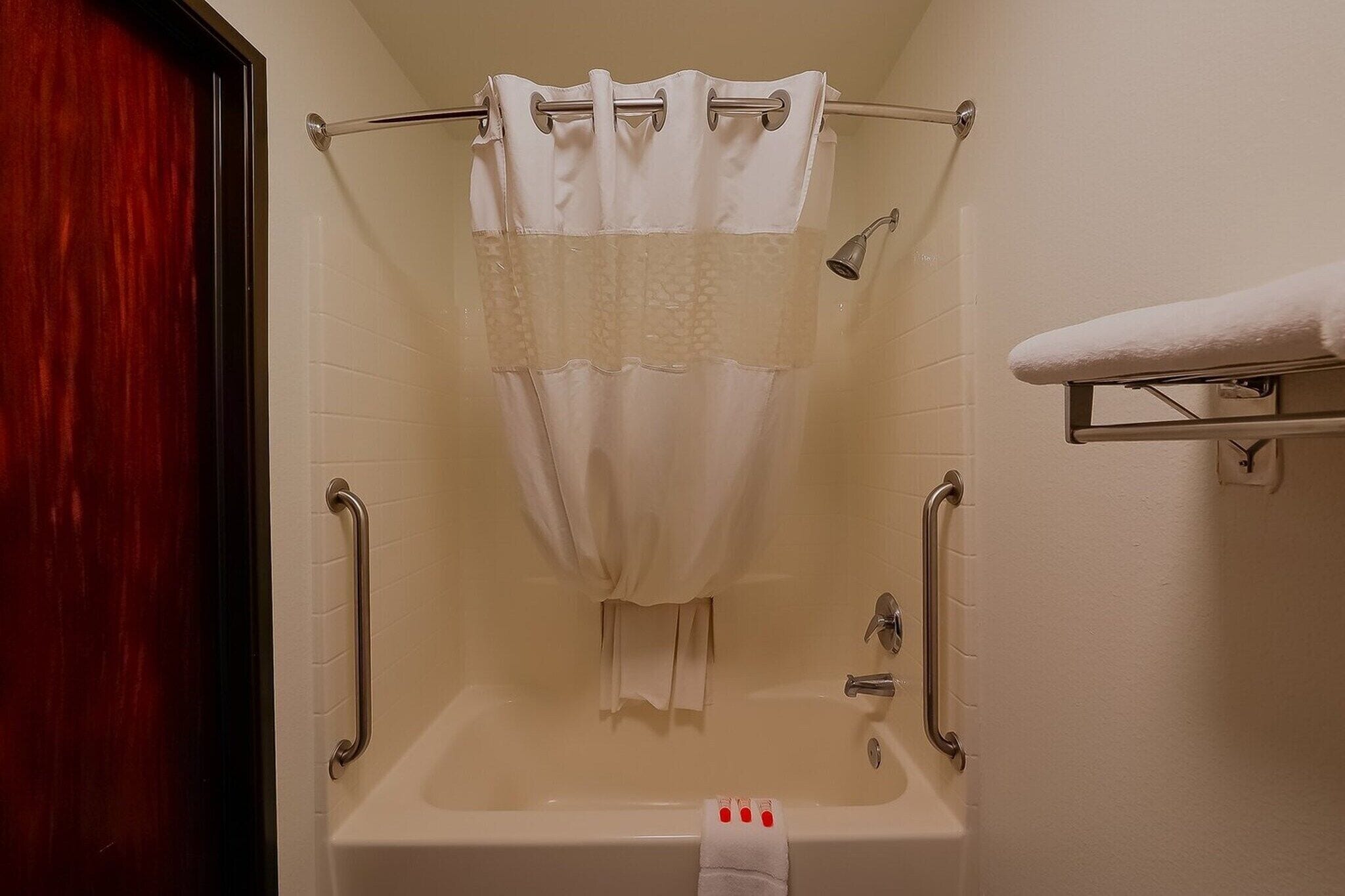 A bathroom with a bathtub, a shower curtain, a towel rack, and a handrail.