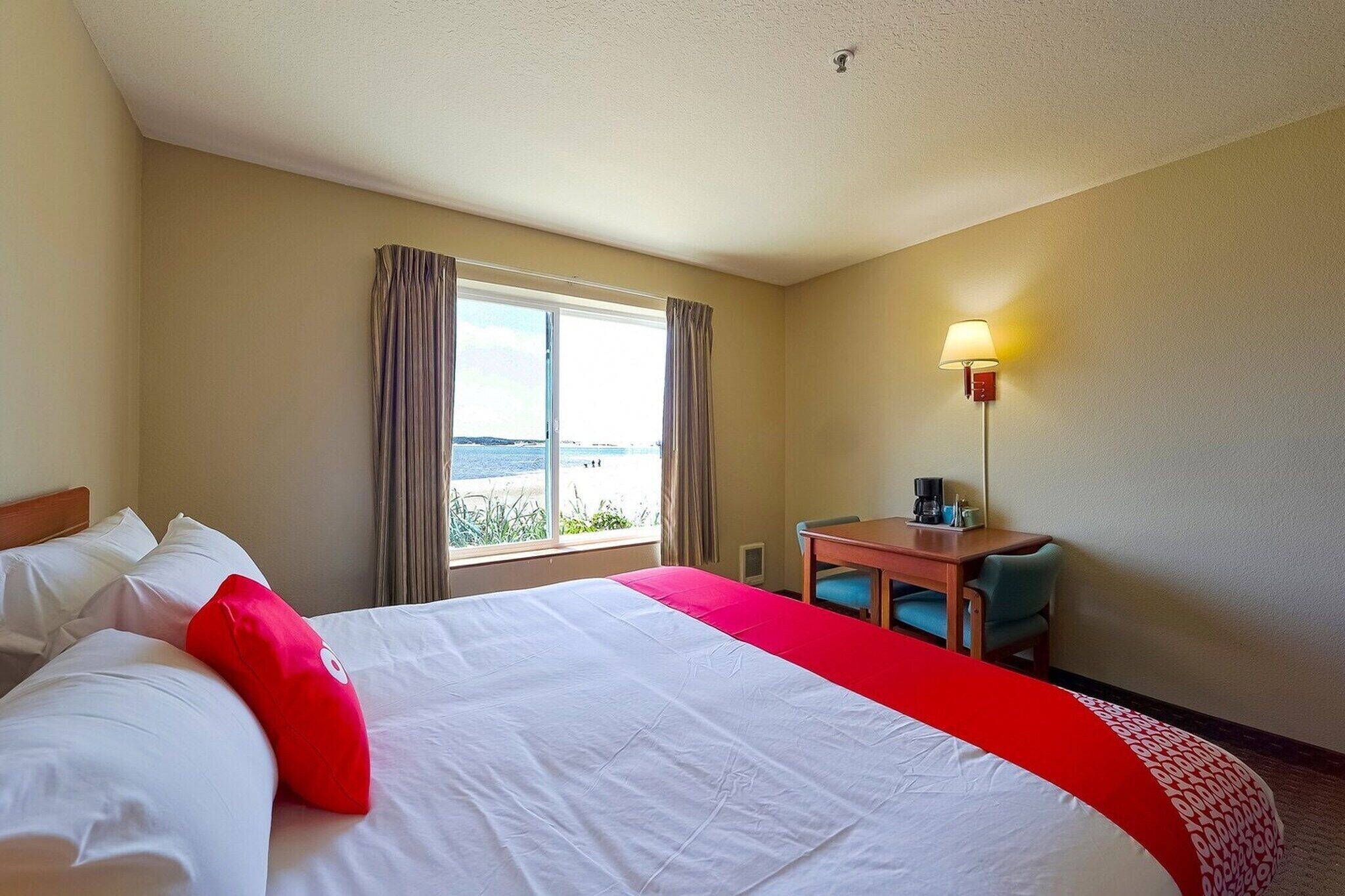 Una habitación de hotel con cama, escritorio, silla, lámpara y ventana con cortinas.