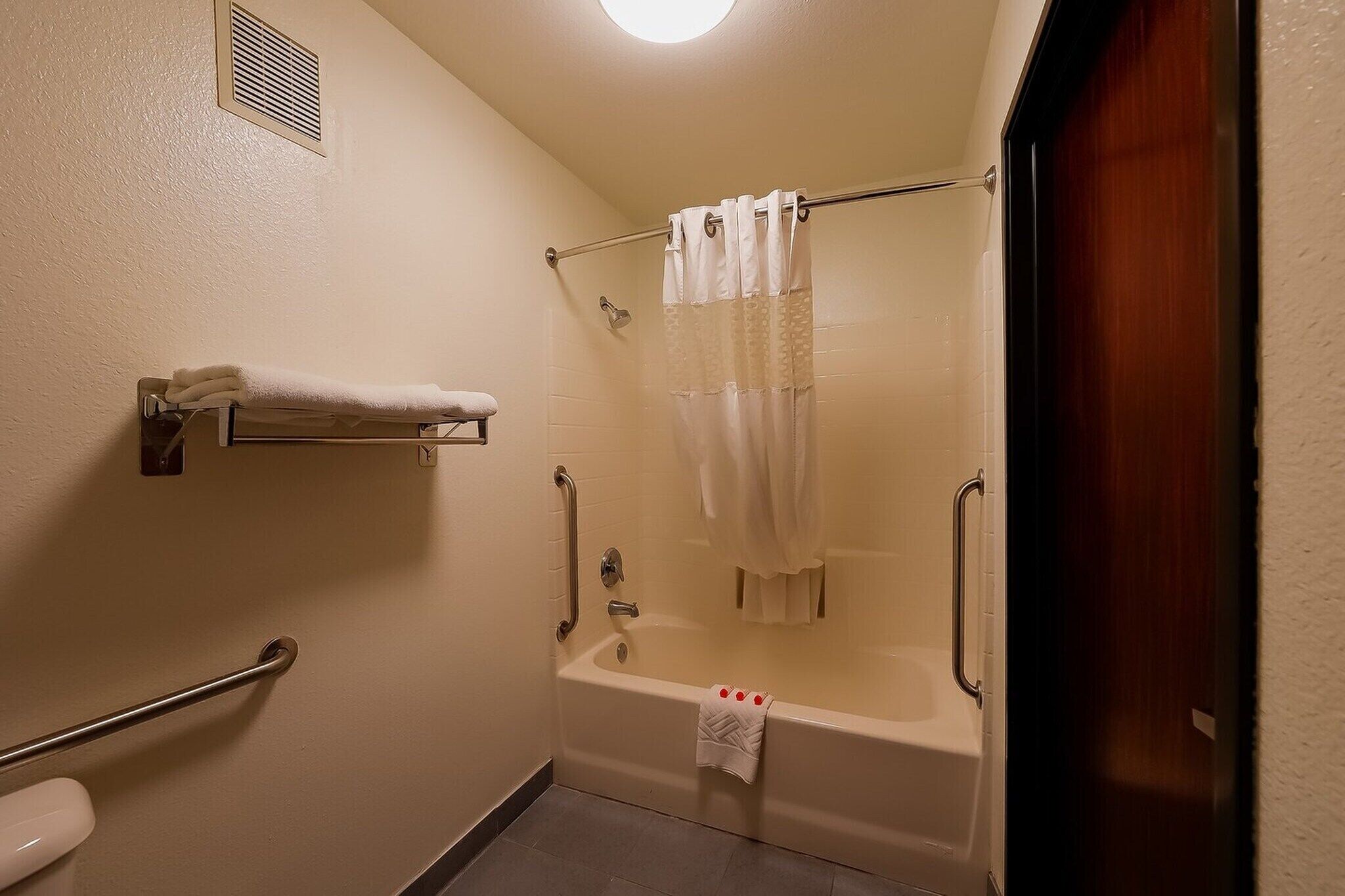Une salle de bain équipée d’une baignoire, d’un rideau de douche, d’un porte-serviettes et d’une barre d’appui.