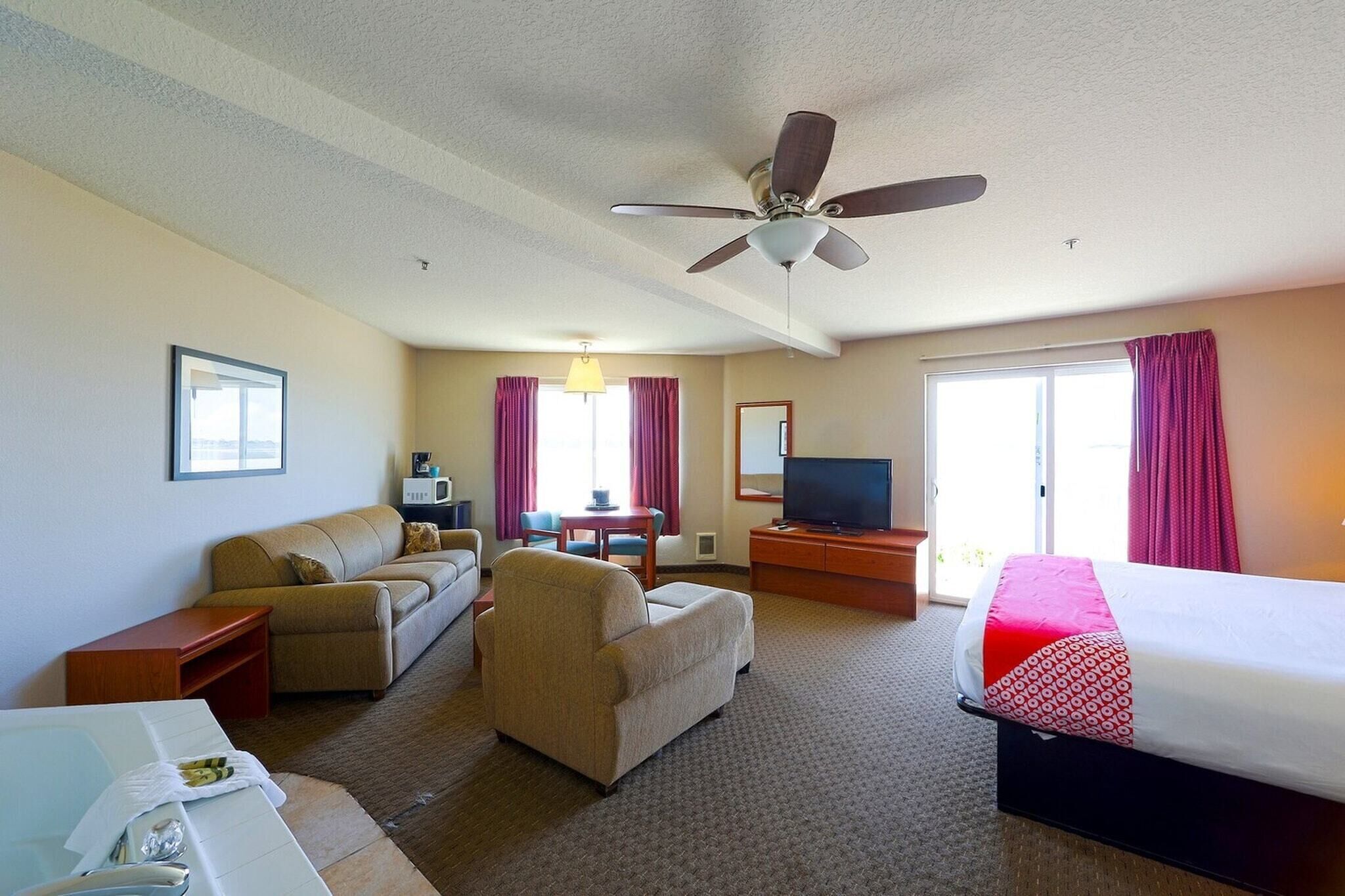 A hotel room with a bed, a sofa, a chair, a TV, a desk, and a ceiling fan.