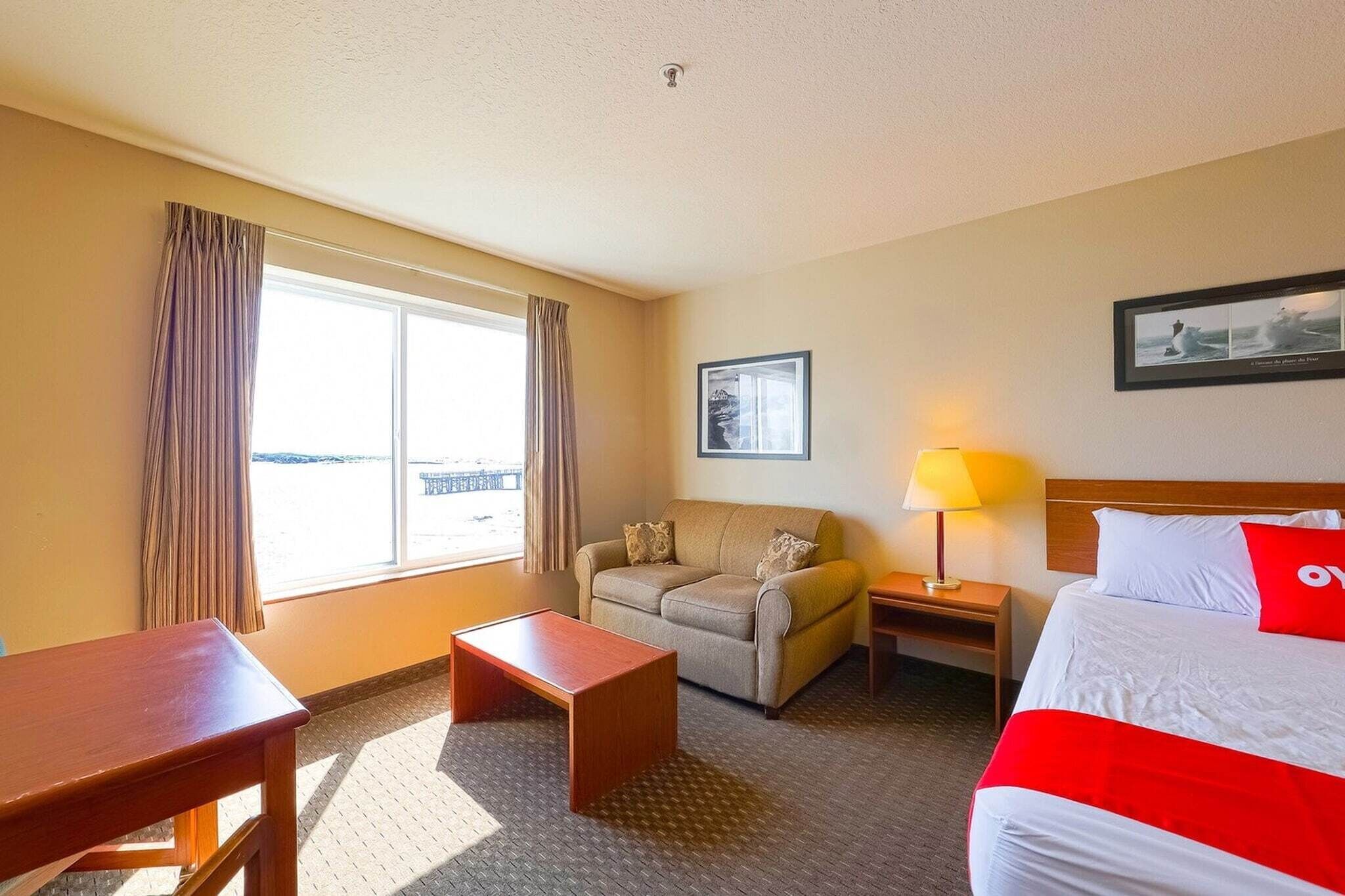 A hotel room with a bed, a sofa, a desk, a lamp, and a window with curtains.