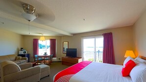 A hotel room with a bed, a desk, a television, a sofa, and a balcony with curtains.
