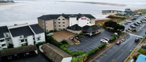 A motel with a parking lot, a road, and a view of the sea.