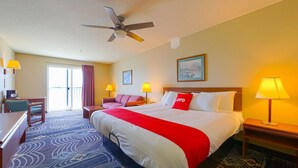 Ein Hotelzimmer mit Bett, Schreibtisch, Stuhl, Sofa, Deckenventilator und einem Fenster mit Vorhängen.