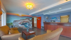 Eine Lobby mit Rezeption, Sitzbereich und einem Wandgemälde, das einen Sonnenuntergang über dem Meer zeigt.