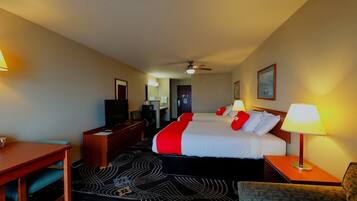 A hotel room with a bed, a desk, a television, a ceiling fan, and a nightstand with a lamp.