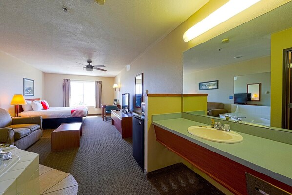 A hotel room with a bed, sofa, desk, TV, and a large bathroom mirror.