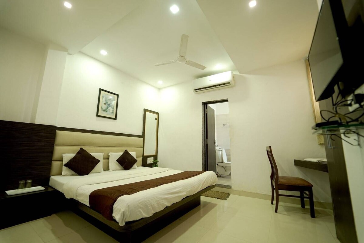 A modern hotel room with a bed, a chair, a TV, and an air conditioning unit.
