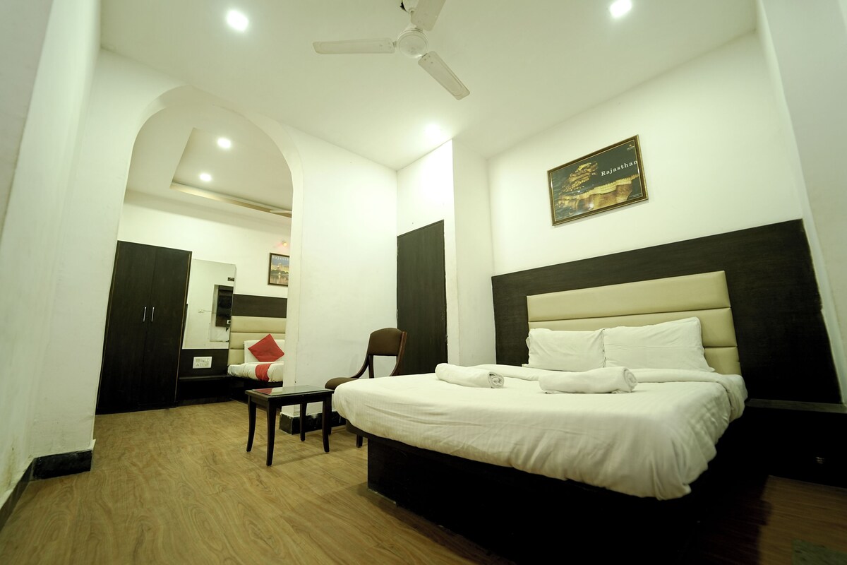 A hotel room with a bed, a desk, a chair, a ceiling fan, and a wall-mounted picture.