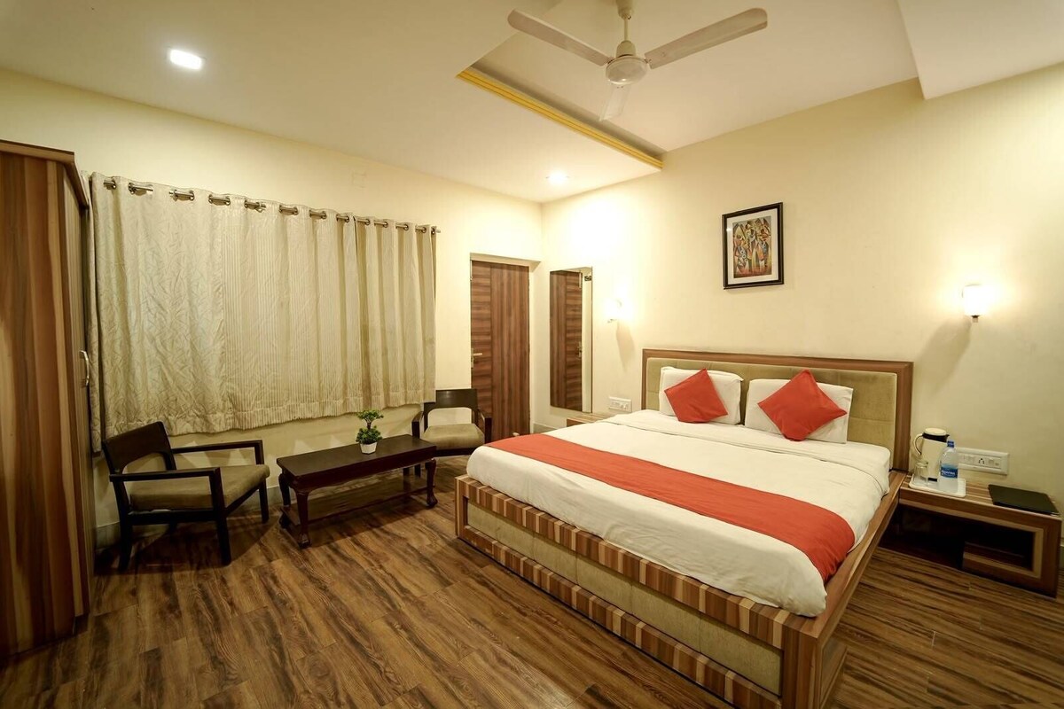 A hotel room with a bed, a desk, a chair, a nightstand, a ceiling fan, and a window with curtains.