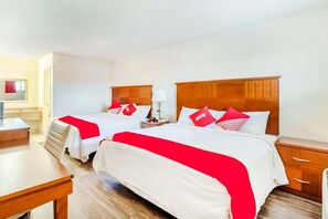 A hotel room with two beds, a desk, a chair, and a nightstand with a lamp.