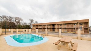 A swimming pool with a wooden deck, a picnic table, and a building with multiple balconies in the background. - 2 King Bed Non Smoking | Antonio Lackland (San-Antonio)