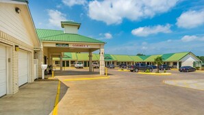 A motel with a green roof, a clear sky, and a parking lot with several cars.