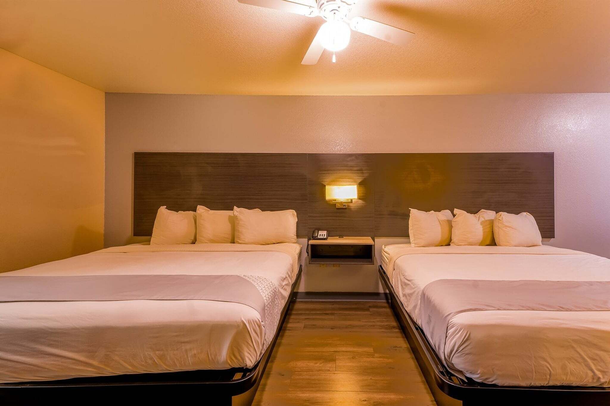 Ein Hotelzimmer mit zwei Betten, einem Deckenventilator, einem Nachttisch mit Lampe und einem hölzernen Kopfteil.