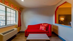 A room with a red sofa, a small table, a window with curtains, and a wall-mounted lamp.