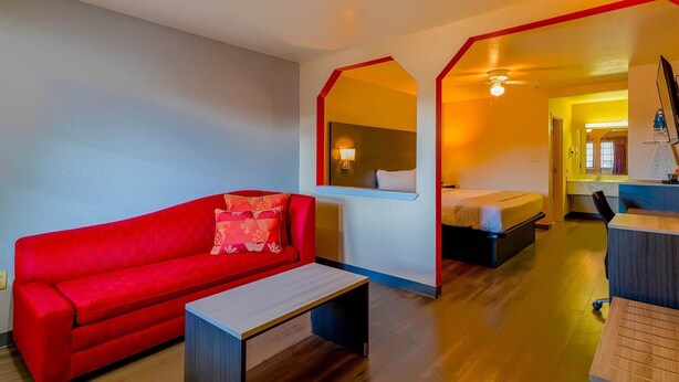 A room with a red sofa, a small table, a bed, and a mirror.