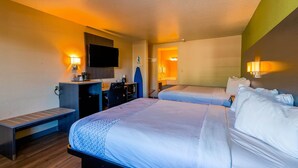 A hotel room with two beds, a desk, a chair, a TV, and a bathroom.