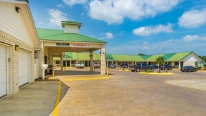 A motel with a green roof, a clear sky, and a parking lot with several cars.
