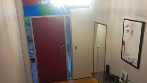 Una escalera con barandillas de madera, una puerta roja y una mesa de vidrio con una planta.
