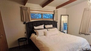 Un dormitorio con cama, ventana, espejo y una mesita.