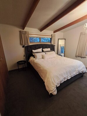 Ein Schlafzimmer mit einem großen Bett, einem kleinen Nachttisch, einem Spiegel und einem Fenster mit Vorhängen.