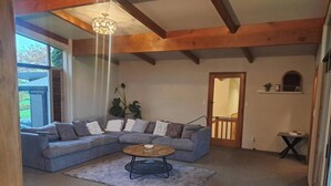 Una sala de estar con un sofá seccional, una mesa de centro redonda, una araña y vistas a través de una ventana.